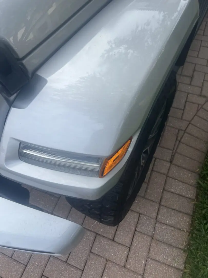 Silver vehicle front corner on brick driveway.