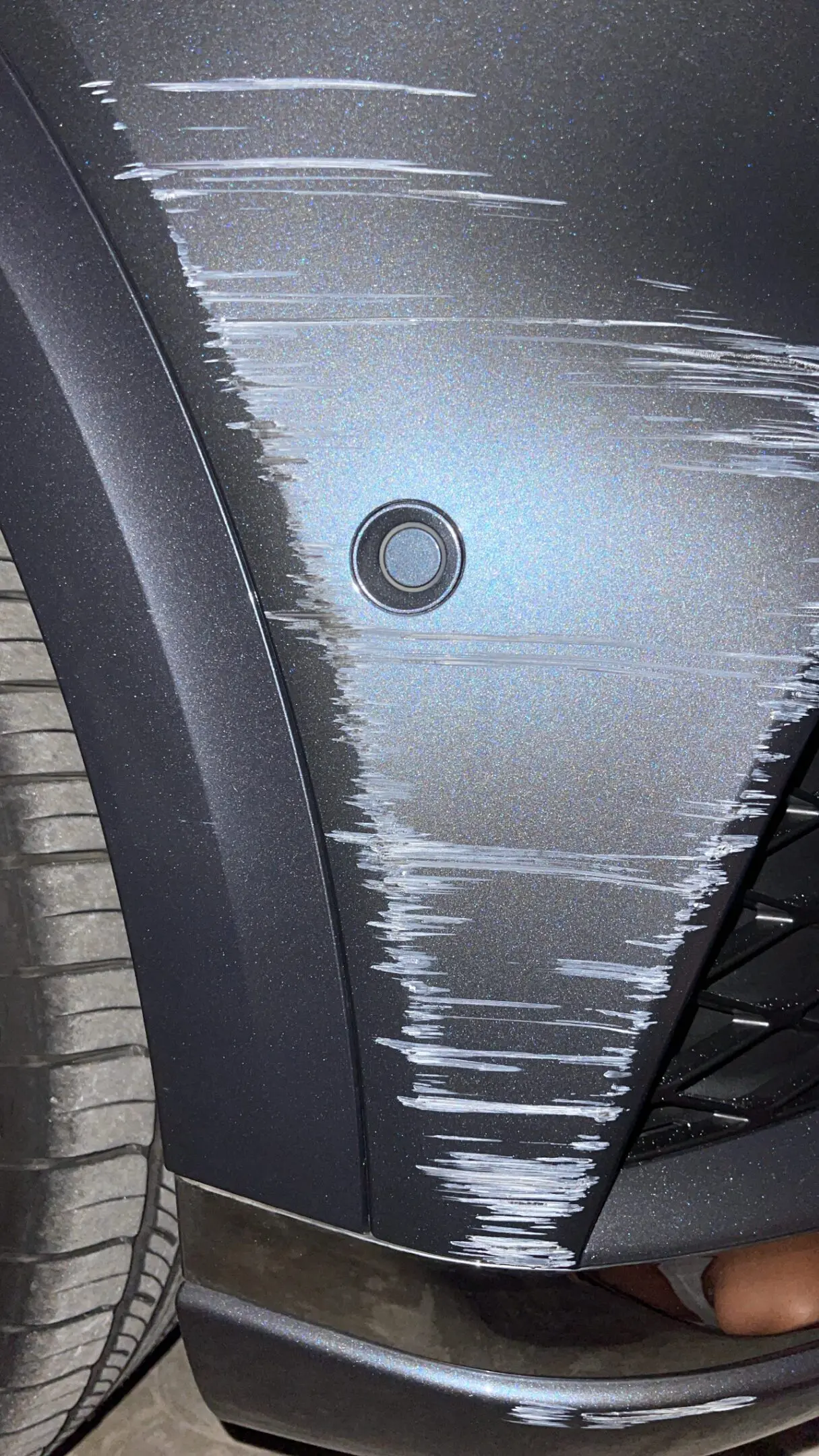 Close-up of a car's scratched side panel near the wheel.