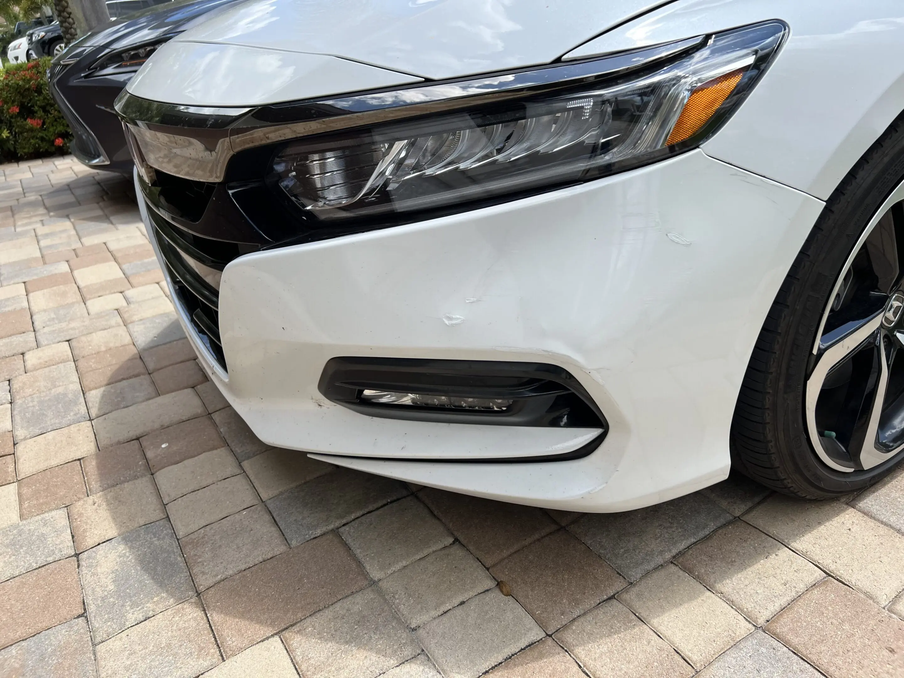 Close-up of a white car's front headlight and fog light on a paved surface.