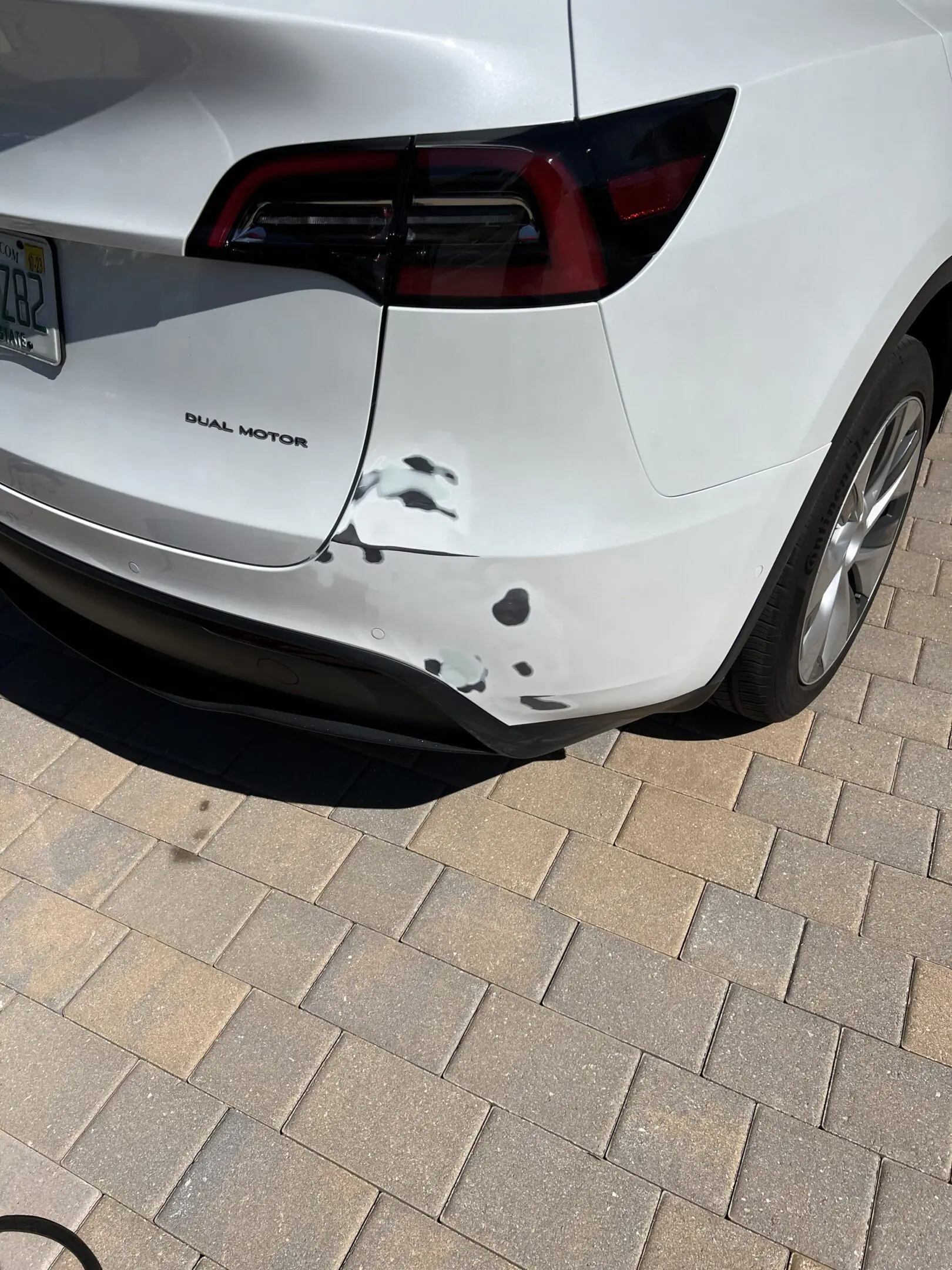 Rear bumper damage on a white car with several scratches and dents.