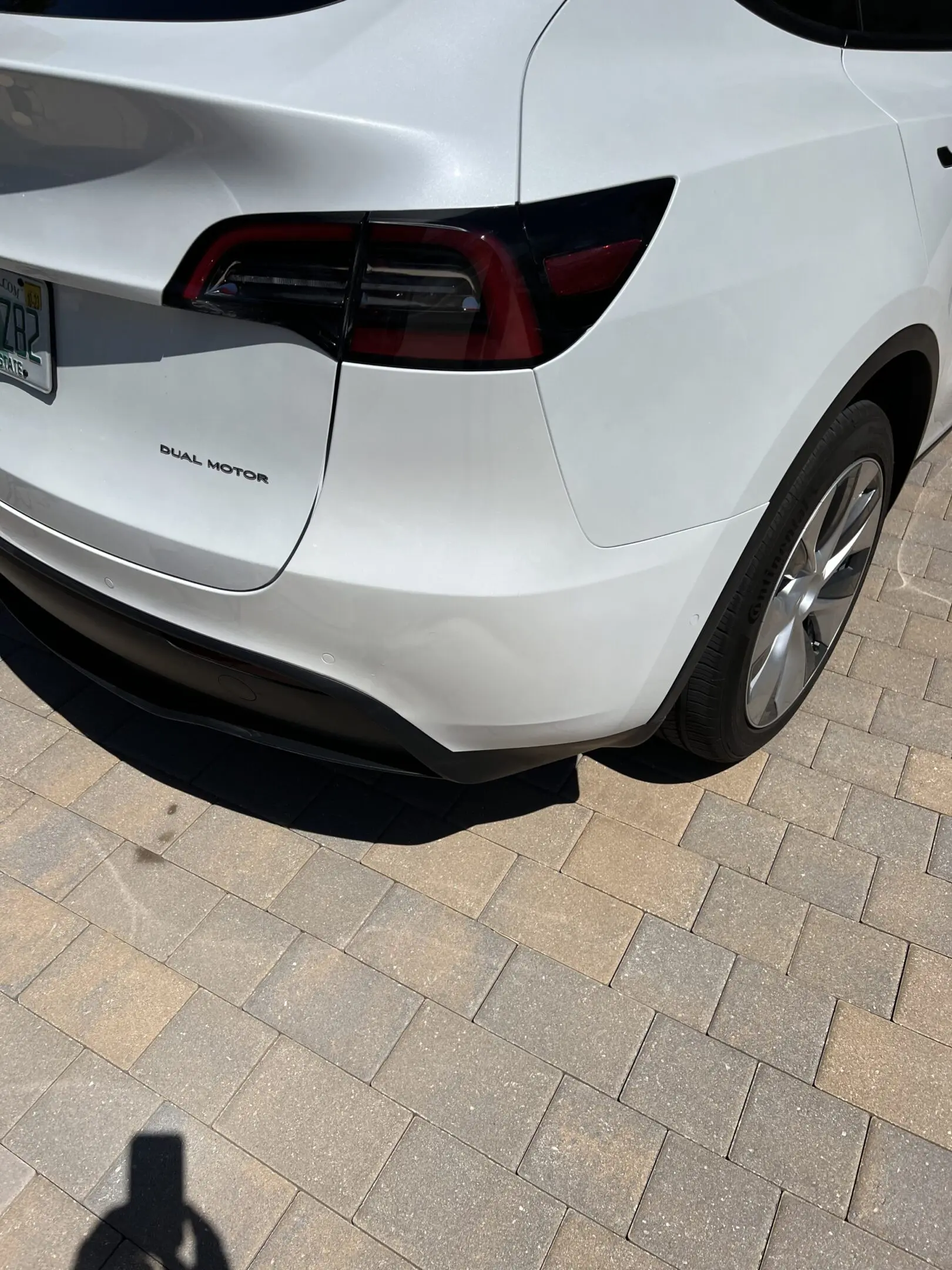 Rear view of a white Tesla Model Y parked on a stone driveway.