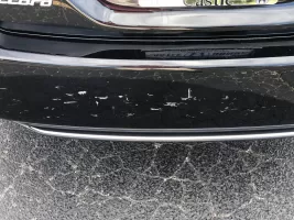 Scratched black car bumper on pavement.